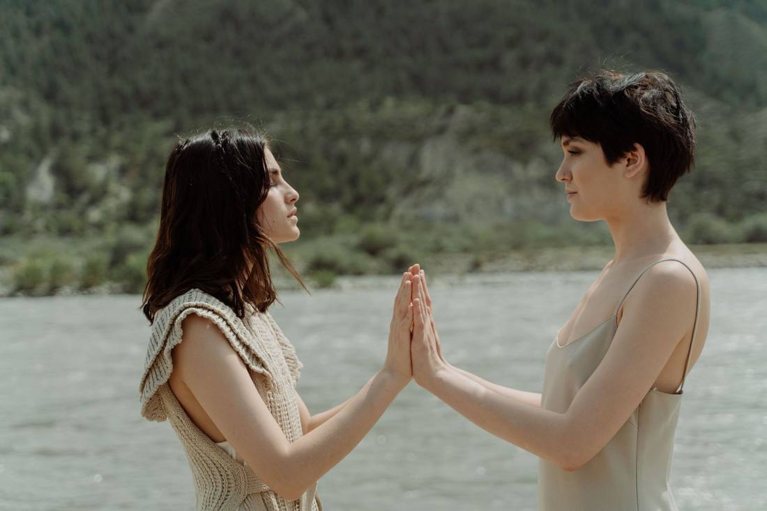 Two women palm to palm by the water